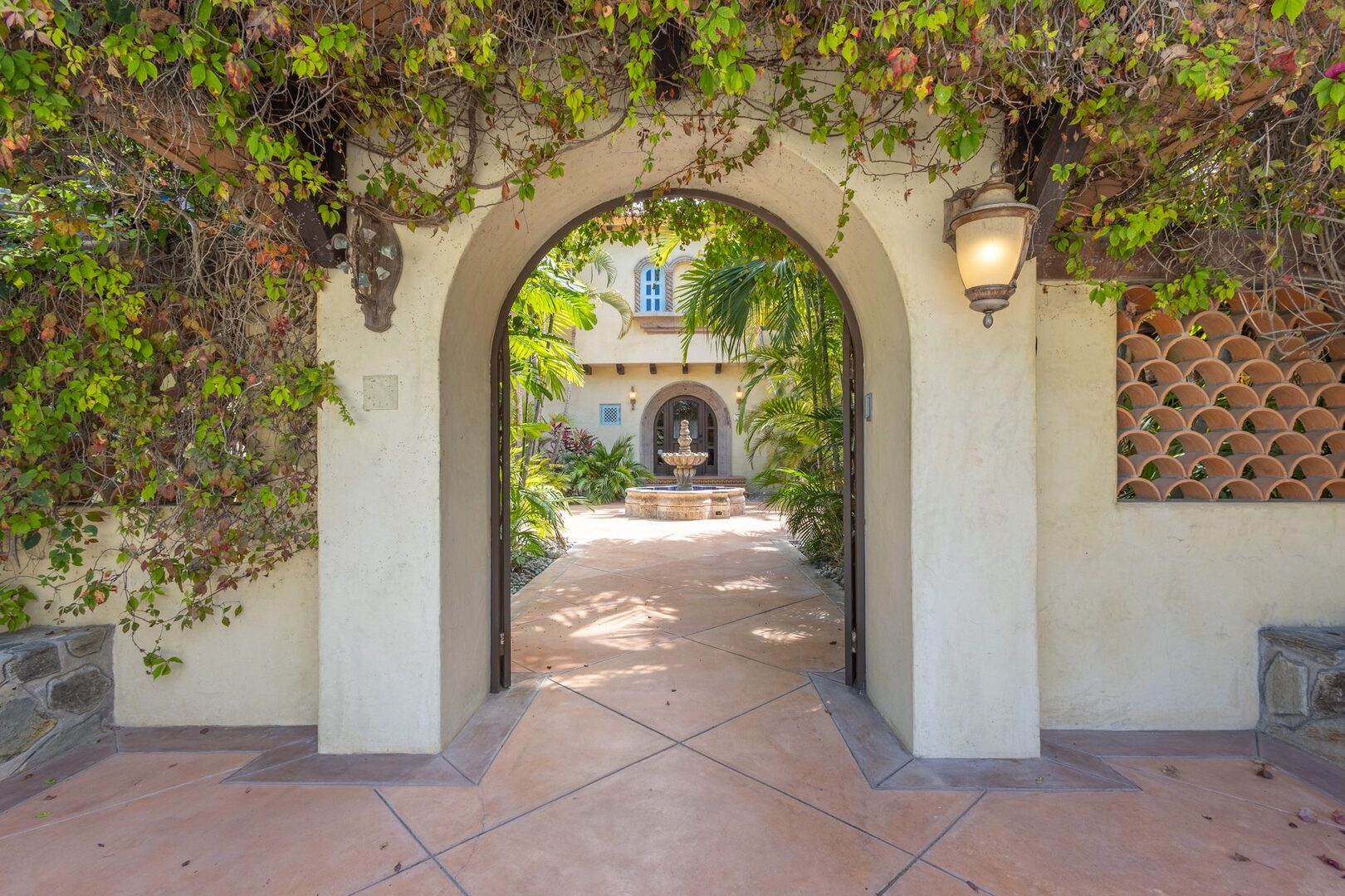 Vine-draped gate arch opening to the courtyard fountain